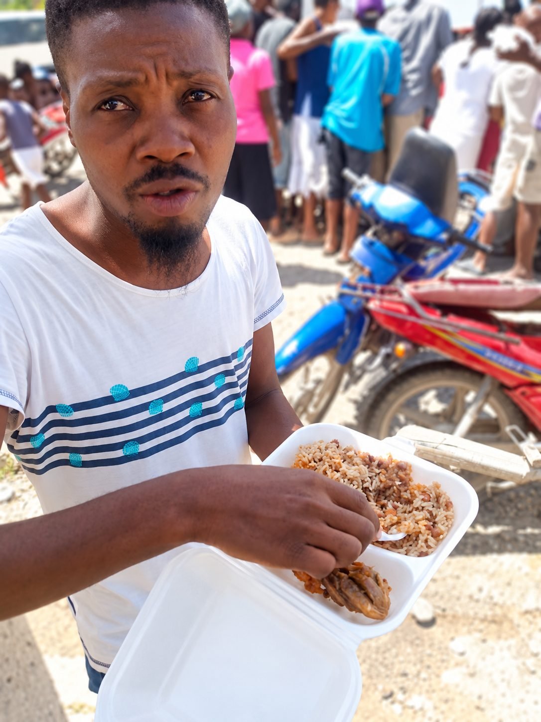 A man holding a plate of rice and beans at a feeding event in Haiti